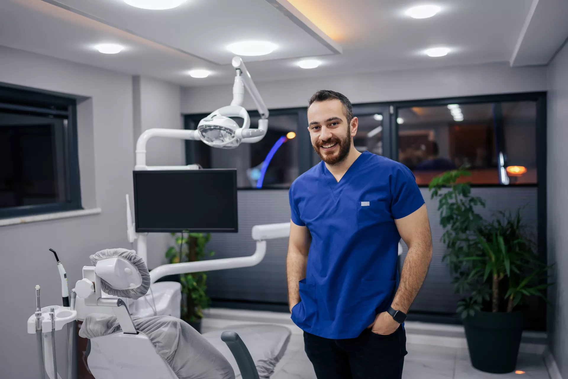 Man in blue shirt standing by dental chair.