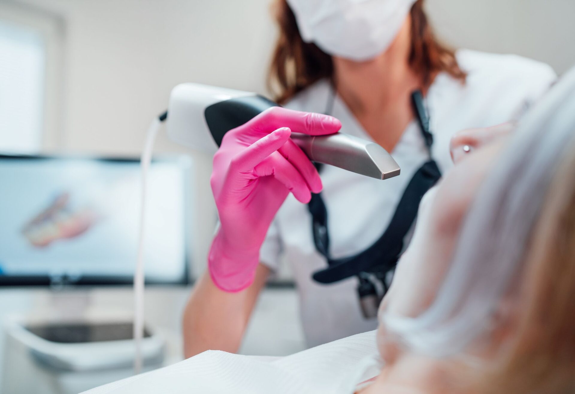 A close-up of a dental professional using an intraoral scanner to capture detailed 3D images of a patient’s teeth. The dentist wears pink gloves and a protective mask while operating advanced scanning equipment, highlighting innovation in digital dentistry.